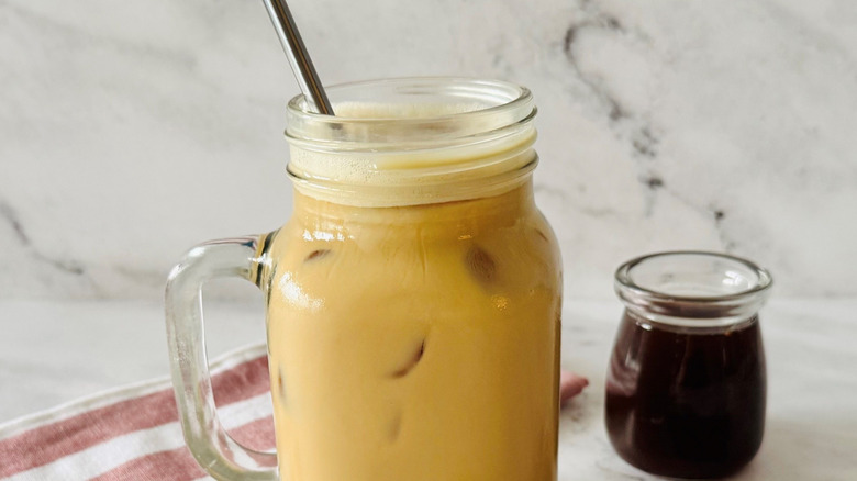 Iced coffee drink in mason jar with bowl of syrup in background