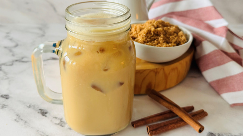 Iced coffee drink in mason jar next to cinnamon sticks