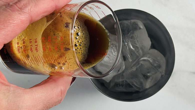 hand pouring coffee into a metal tumbler