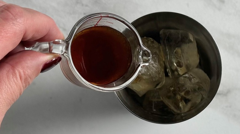 hand pouring syrup into a metal tumbler
