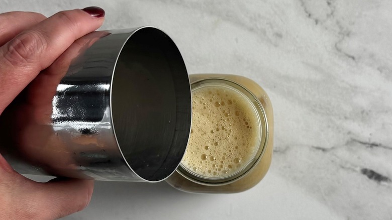 hand pouring a drink out of a lidded metal tumbler
