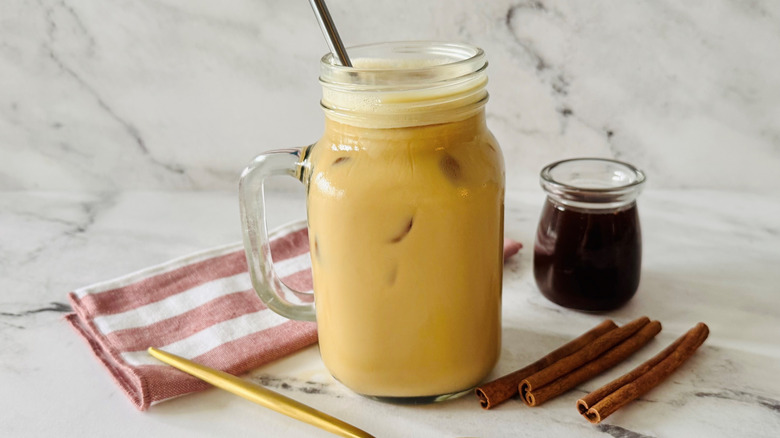 coffee drink in a mason jar-style mug posed next to cinnamon sticks