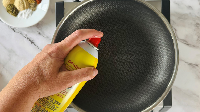 hand holding a spray can over a frying pan