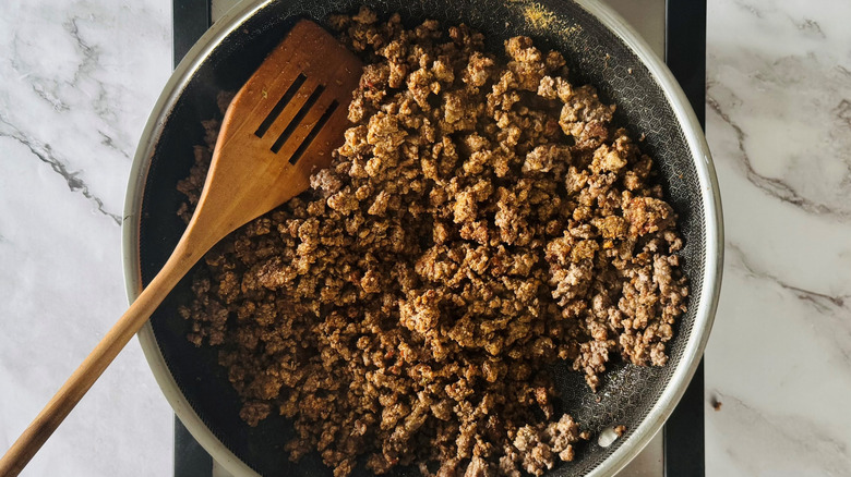 cooked ground beef in a frying pan with a wooden spatula