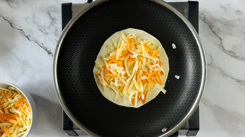 flour tortilla topped with shredded cheese in a frying pan