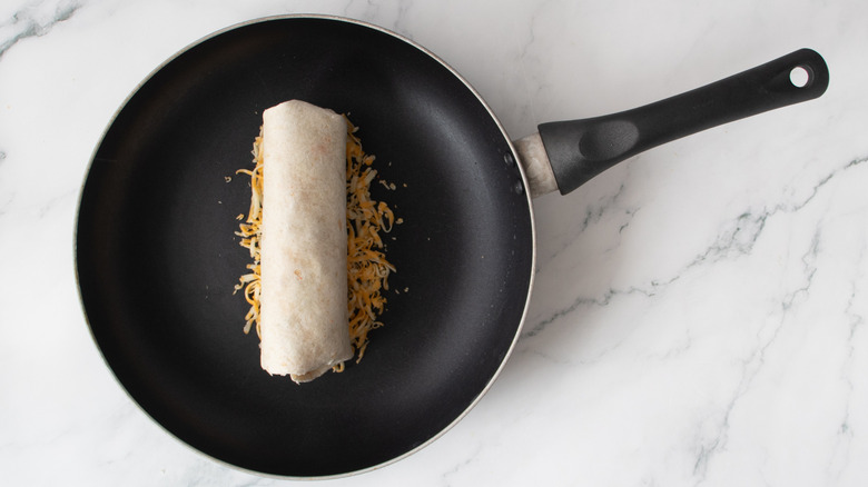 burrito and shredded cheese in a black frying pan