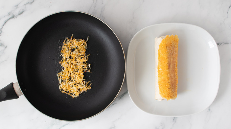 orange and white burrito next to a black frying pan filled with shredded cheese