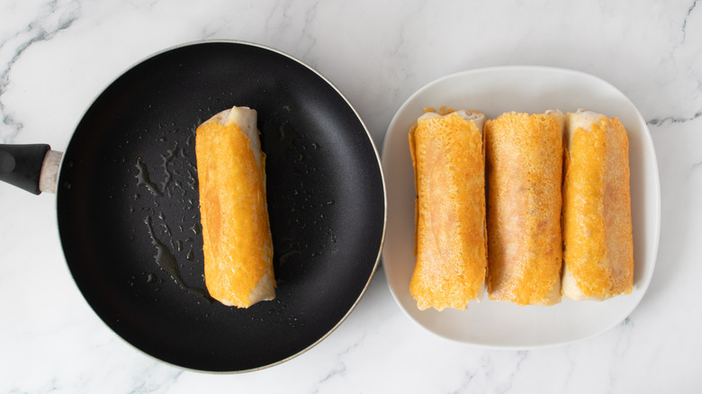 orange-colored burritos next to or in a black frying pan