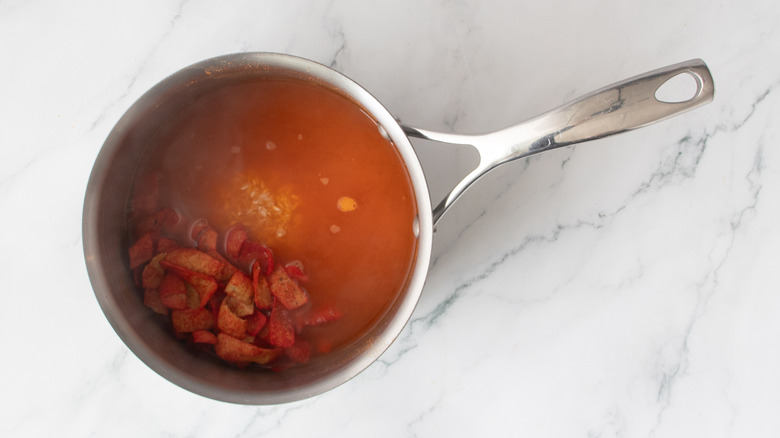 brownish-red liquid in a metal pot with partially submerged stuff in it