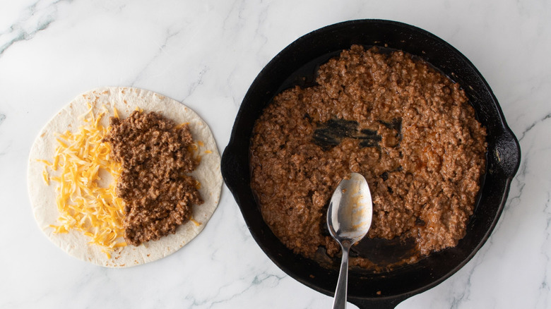 Cheese and beef taco next to skillet with beef