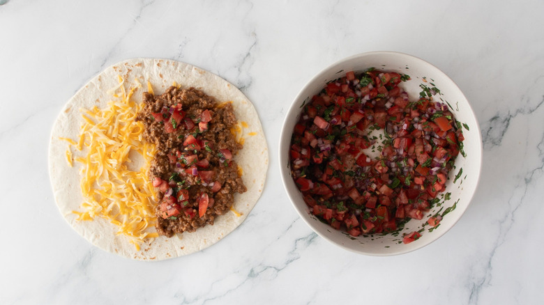 Taco with cheese, beef, and salsa next to bowl of pico de gallo