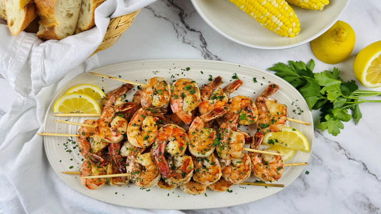 grilled skewered shrimp on platter with corn and bread