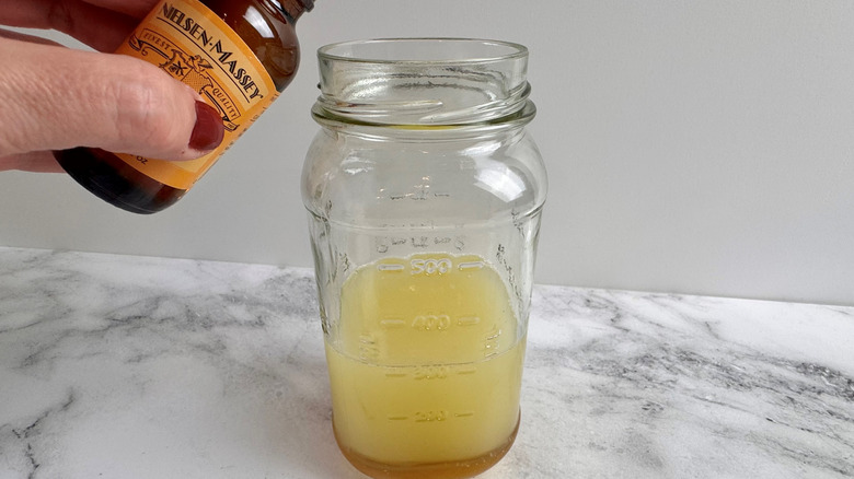 hand holding a bottle over a jar of lime juice