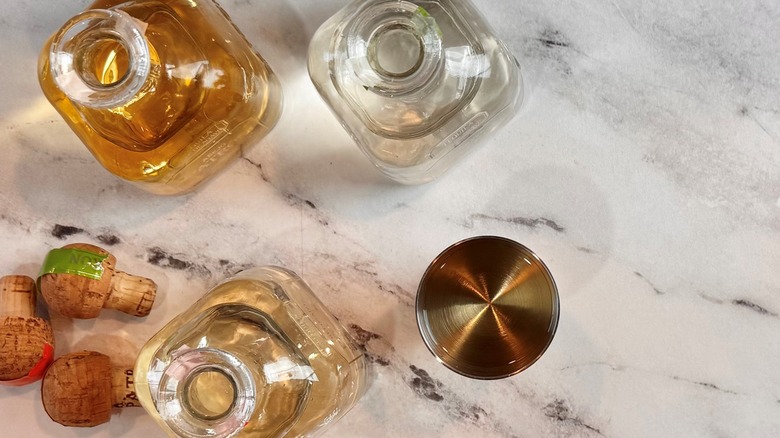 three bottles of liquid next to a metal tumbler