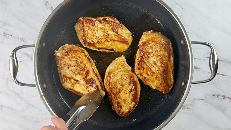 Tongs flipping chicken breast in pan