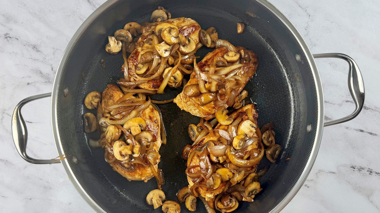 Chicken covered with onion and mushroom mixture in pan