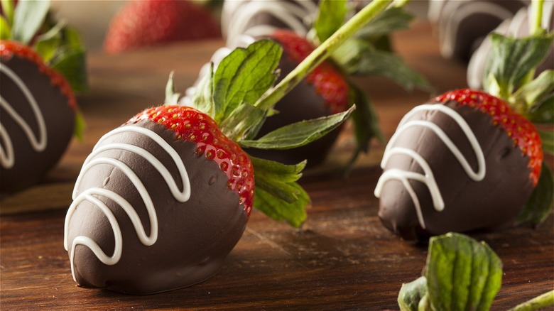 Chocolate-covered strawberries drizzled with white chocolate on a wooden surface