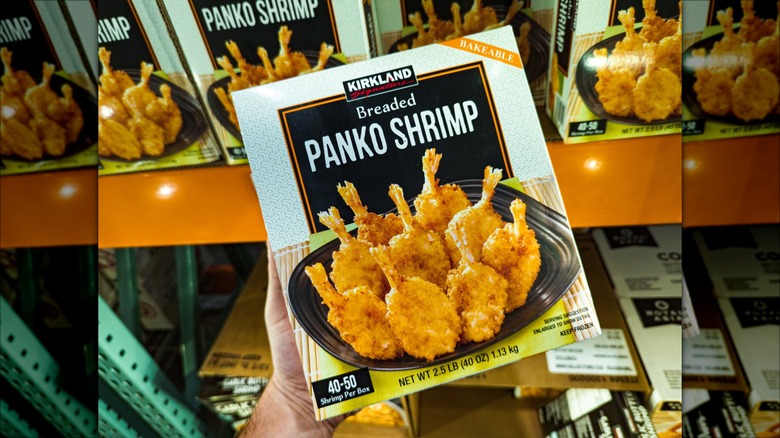 Hand holding box of Kirkland Signature breaded panko shrimp inside Costco.