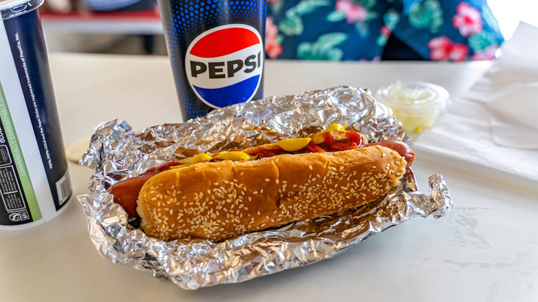 Costco hot dog with bun, mustard, and ketchup sitting on table with beverages.