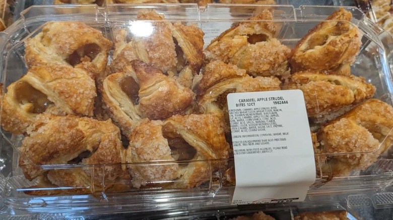 A plastic container filled with pastry knots covered in sugar and filled with apple filling.