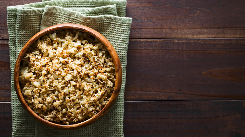 Bowl of riced cauliflower with green napkin on wooden table