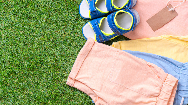 Pastel colored clothes and brightly colored sandals laid out on the grass