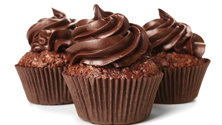 Three chocolate cupcakes with frosting on white background