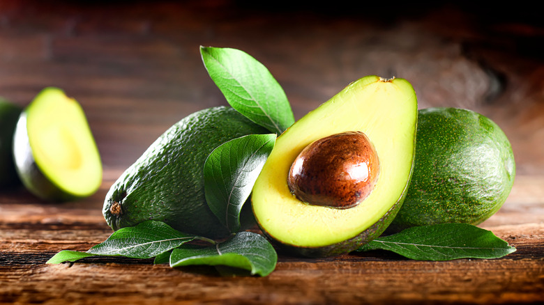 Whole and halved avocados and leaves on table