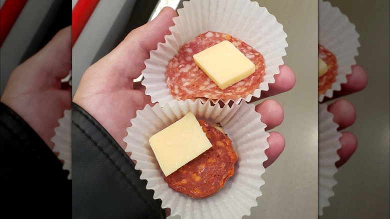 Person's hand holding two samples of meats and cheese