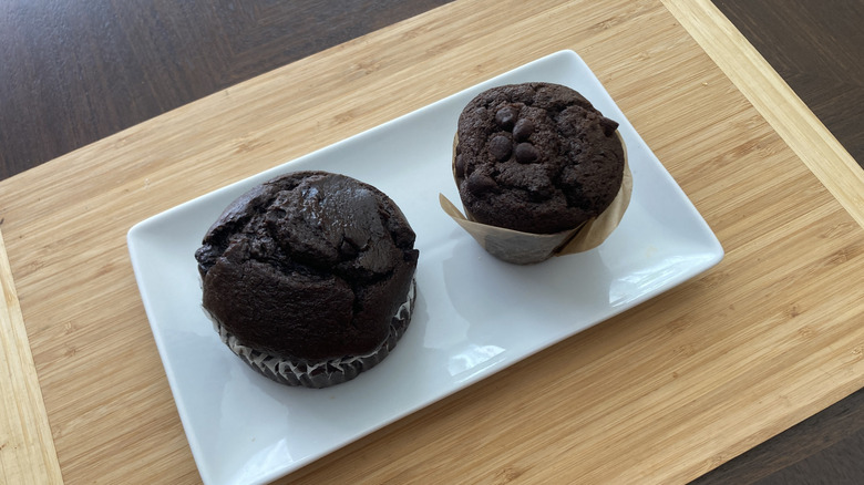 Two chocolate muffins sit on a rectangular white plate on a wooden background.