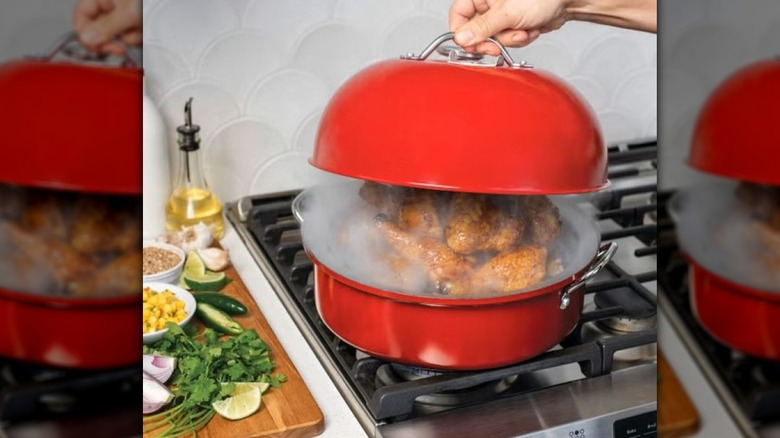 Lid being lifted off a red Kettle Smoker showing smoking coming out of it with chicken inside
