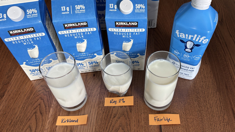 Top view of three cartons of Kirkland Signature ultra-filtered milk, a bottle of Fairlife ultra-filtered milk, a glass of each, and a glass of 2% milk