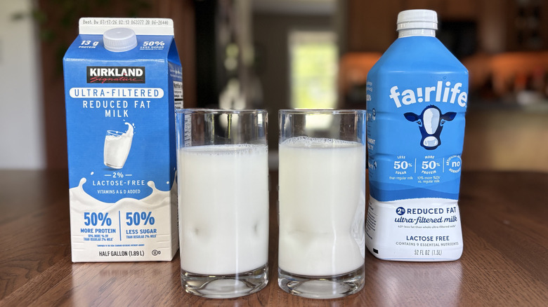 Cartons of Fairlife and Kirkland Signature ultra-filtered milk with glasses of milk beside each one