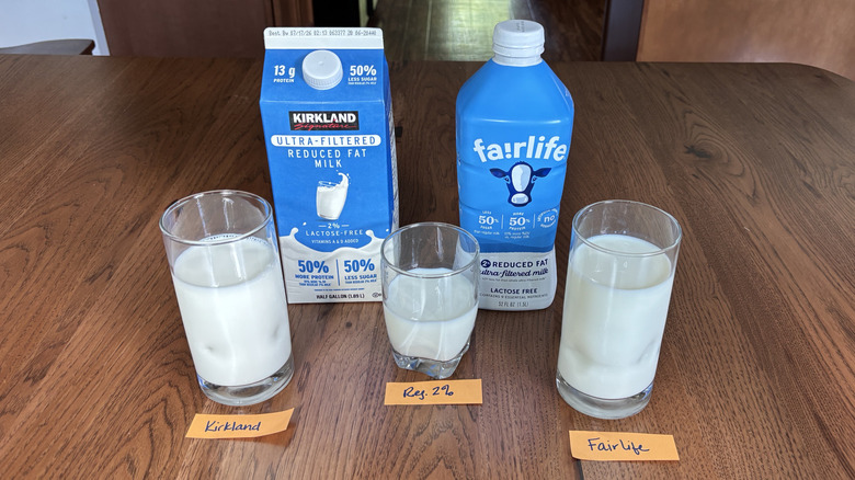 Carton of Kirkland Signature ultra-filtered milk and a bottle of Fairlife ultra-filtered milk with a glass of each and a glass of regular 2% milk