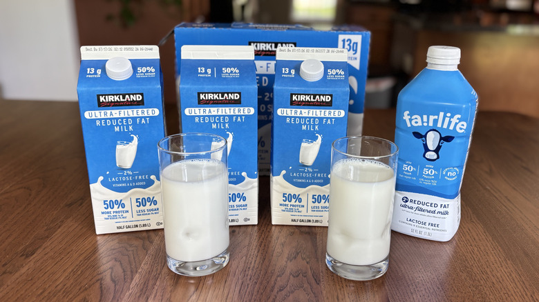 Three cartons of Kirkland Signature ultra-filtered milk and a bottle of Fairlife ultra-filtered milk with two full glasses of milk in the front
