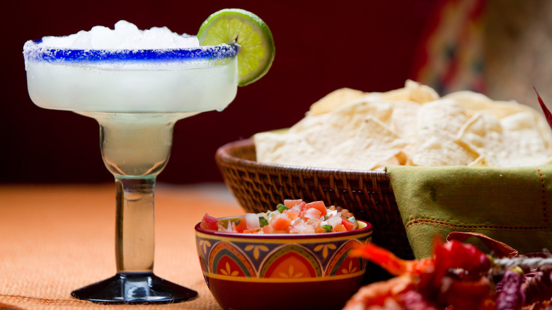 A frozen margarita with lime next to chips and salsa.