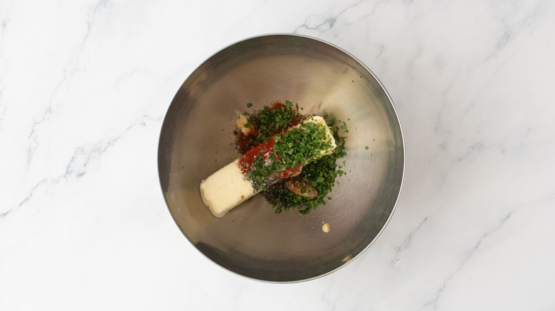 Stick of butter, herbs, and seasonings in a bowl