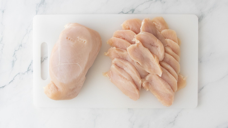 Whole chicken breast and chicken slices on cutting board