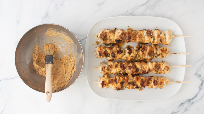 Bowl of cowboy butter next to grilled chicken skewers on plate