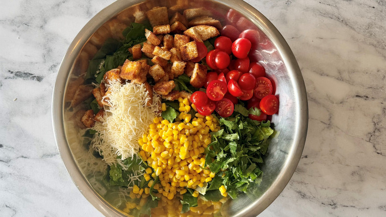 Lettuce, corn, croutons, tomatoes, and parmesan in bowl