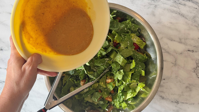 Dressing pouring into bowl with lettuce and tongs