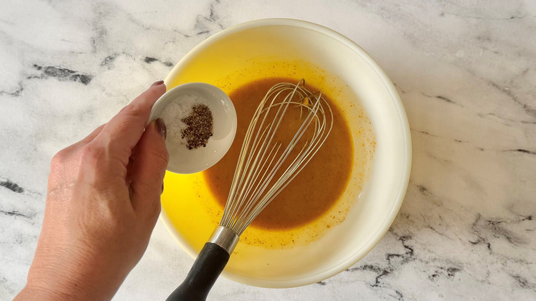 Hand adding salt and pepper to bowl of dressing with whisk