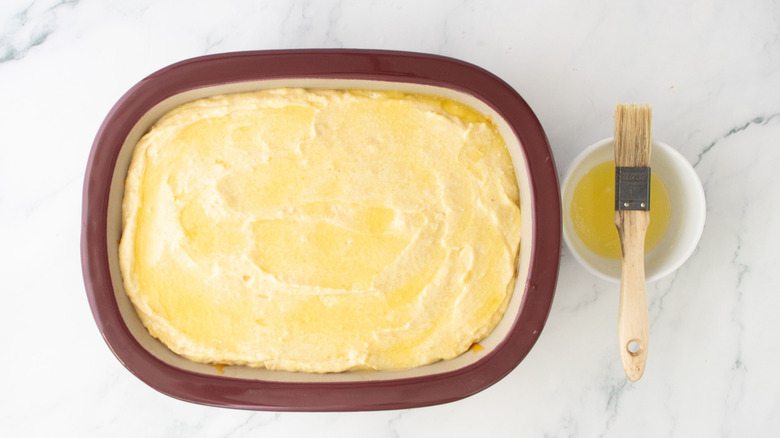 Unbaked cornbread in casserole dish topped with melted butter