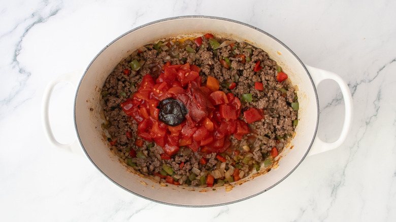 Beef mixture topped with diced tomatoes and tomato paste in Dutch oven