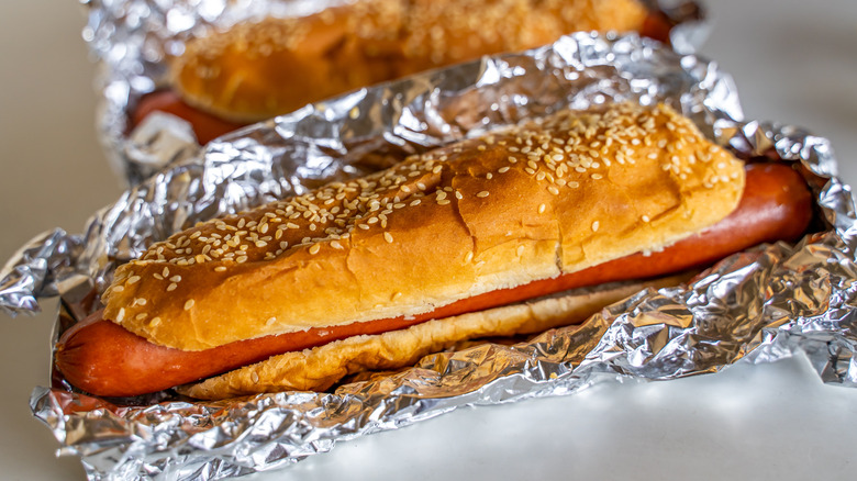 A Costco hot dog wrapped in aluminum foil sitting on a table in the food court