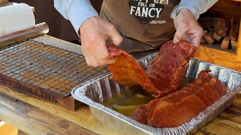 Kent Rollins placing a rack of ribs in a foil pan with chicken broth.