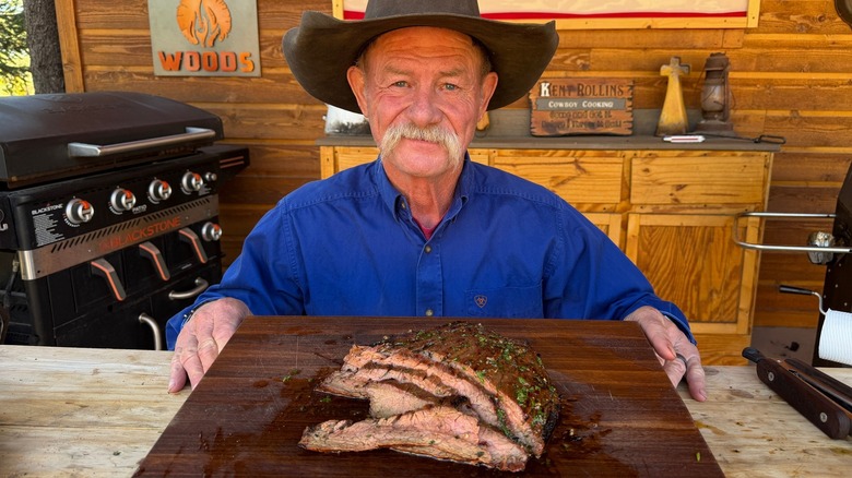 Cowboy Kent Rollins posing with sliced meat on a cutting board