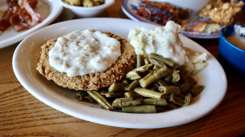country fried steak with gravy green beens and potatoes on plate
