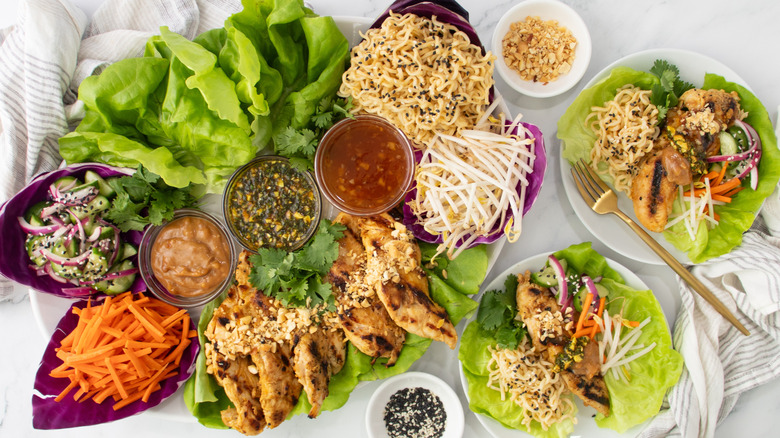 Chicken lettuce wraps with various vegetable toppings and bowls of sauces