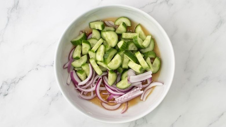 Cucumber salad with red onion in white bowl